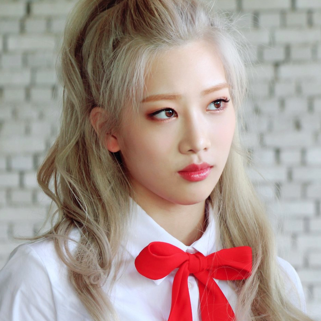 Kim Lip from the 'Eclipse' music video. She has long blonde hair and is wearing a white shirt with a red bow. She is staring off into the distance.